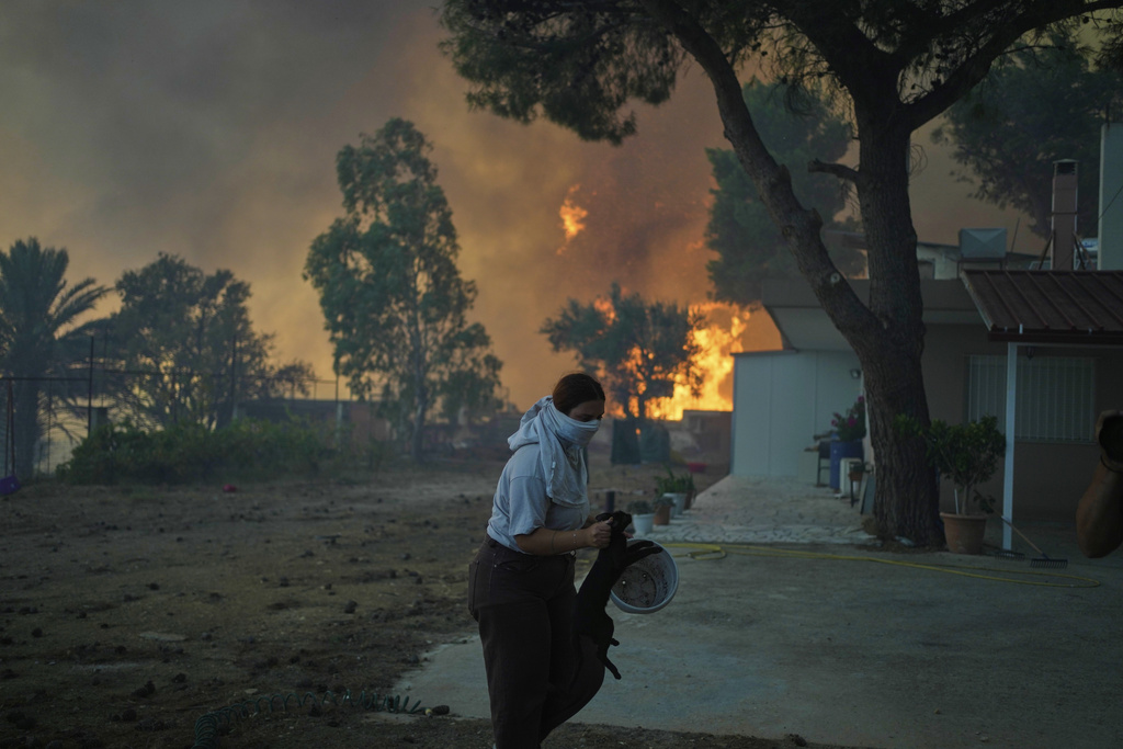 A woman takes away a cat as the fire approaches a house during a wildfire in Patras city, western Greece, Wednesday, Aug. 13, 2025. (AP Photo/Thanassis Stavrakis)